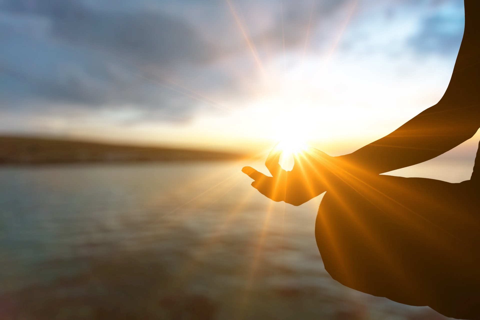 Hands in meditation pose silhouetted against a sunset over water